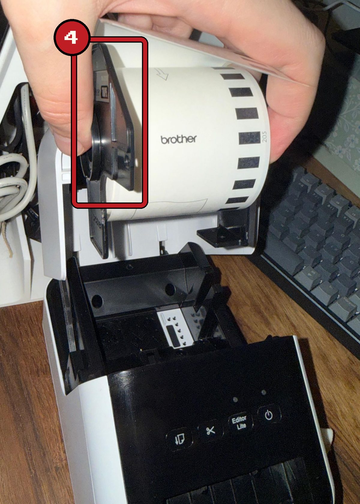 Eine Hand setzt eine neue Brother-Rolle von oben in den geöffneten Drucker ein, die schwarzen Seitenteile der Rolle sind rot markiert