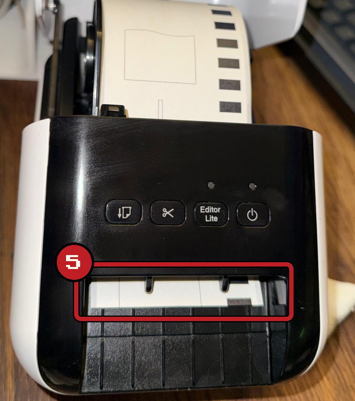 Draufsicht auf den Drucker: Der Papieranfang schaut vorne aus dem Auswurfschlitz, der Schlitz ist rot markiert
